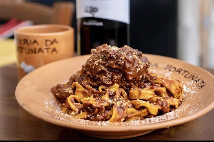 En tallerken med pasta servert med kjøttsaus og revet ost, ved siden av en flaske vin og en kopp.