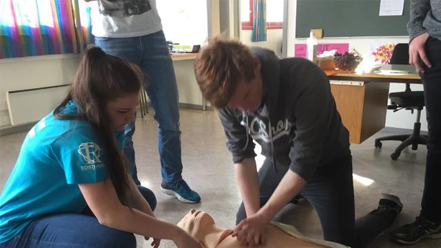 To unge mennesker utfører hjerte-lunge-redning på en dukke i et klasserom.