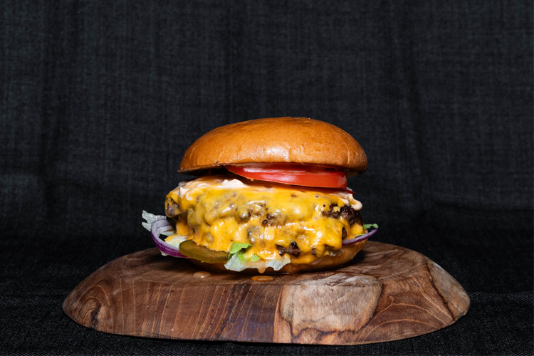 Saftig cheeseburger med smeltet ost, tomat, salat og rødløk på en treplate.