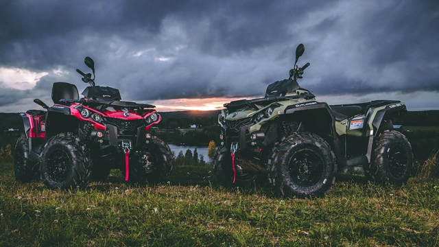 To ATV-er parkert på en grønn eng med dramatisk himmel og solnedgang i bakgrunnen.