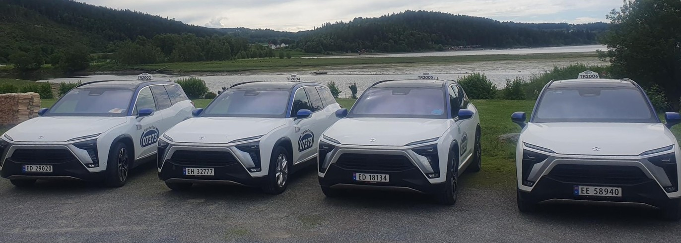 Fire hvite SUV-er parkert ved en innsjø, med blå detaljer og landskap i bakgrunnen.