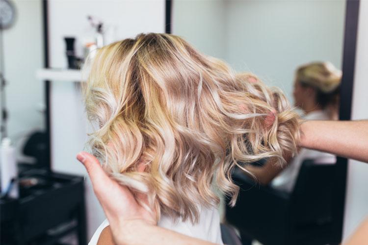 En frisør styler en kundes bølgete, blondt hår i en moderne salong.