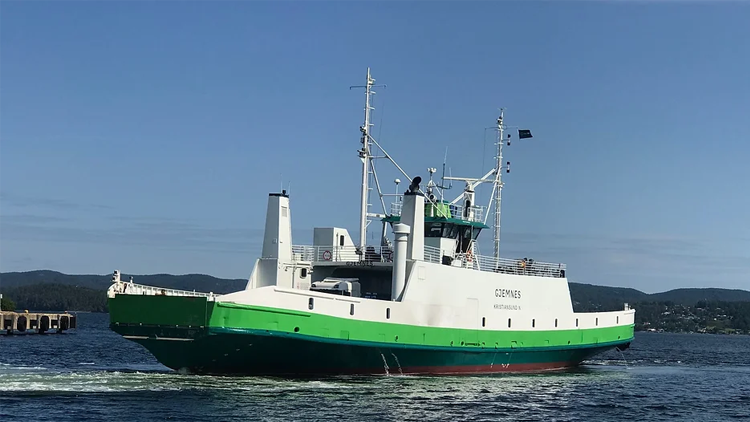 Ferge med grønn og hvit farge seiler på vannet under en klar blå himmel.
