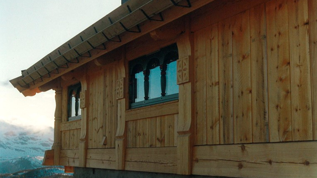 En trehytte med utskårne detaljer og vinduer, plassert i fjellandskap.