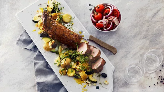 Saftig stek med poteter, grønnsaker og en frisk salat med tomater og løk på et serveringsfat.
