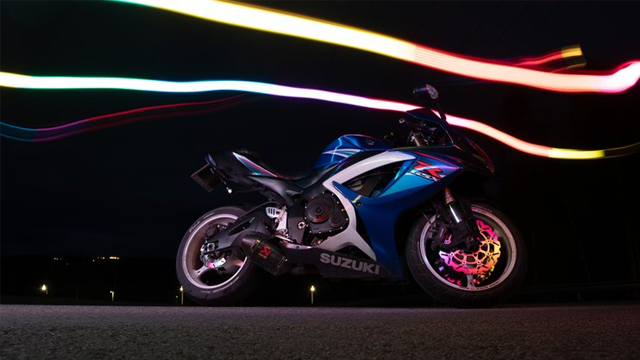 En blå Suzuki motorsykkel med lysstriper i bakgrunnen, fotografert om natten.
