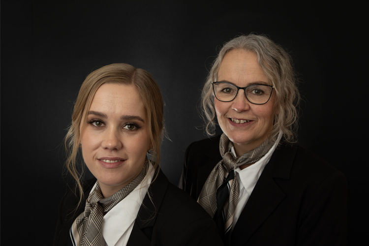 To kvinner i formelle klær med skjerf, poserer foran en svart bakgrunn.