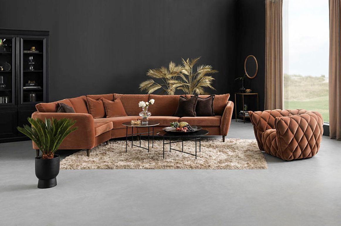 Moderne stue med en brun sofa, en tuftet lenestol, et svart bord og planter mot en mørk vegg.