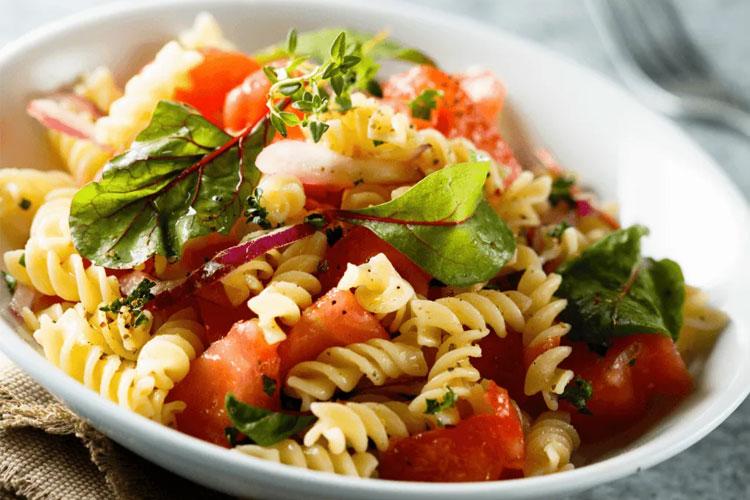 En tallerken med pastasalat med fusilli, tomater, urter og grønne blader.