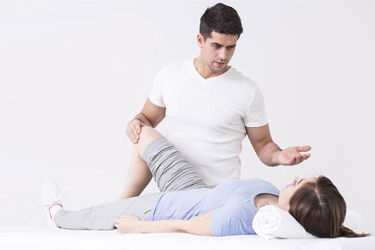 En fysioterapeut gir behandling til en kvinne som ligger på en benk med en pute under hodet.