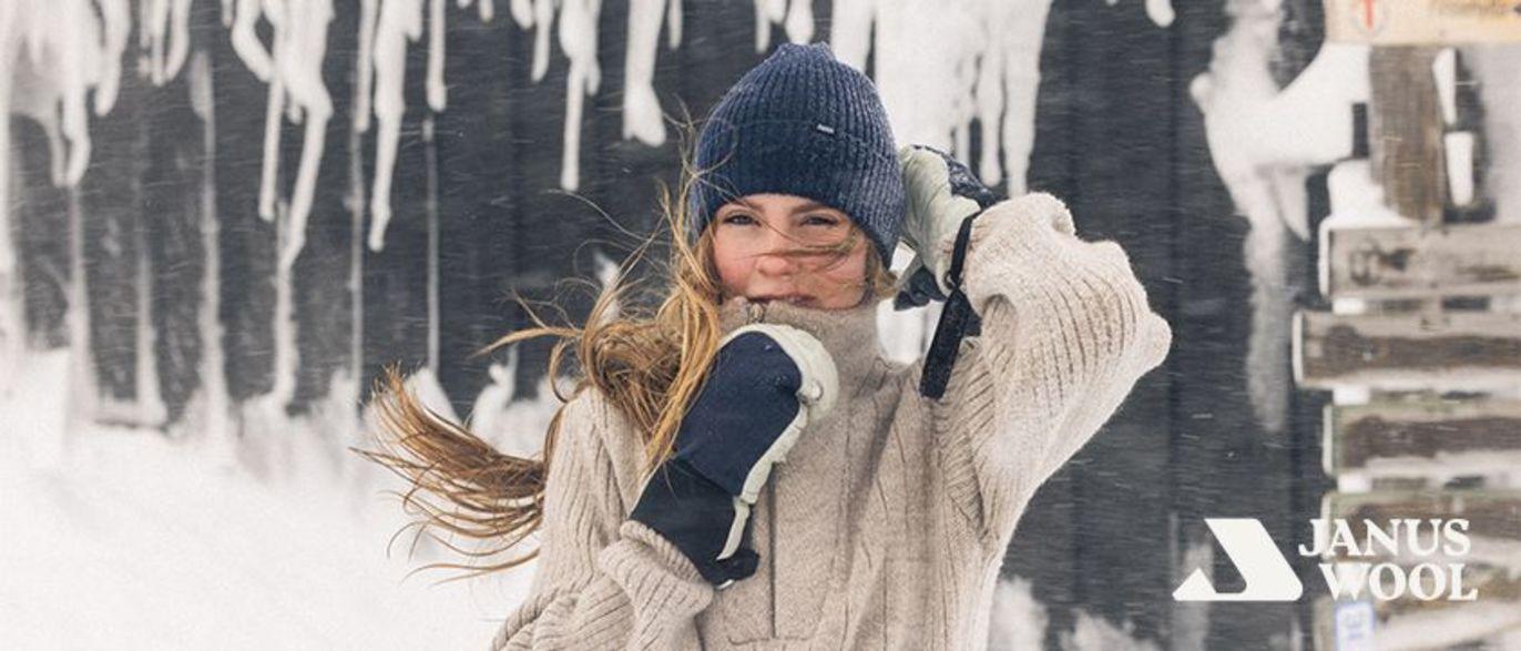 Jente i vinterklær med lue og votter, smilende i snøen med is på treverket i bakgrunnen.