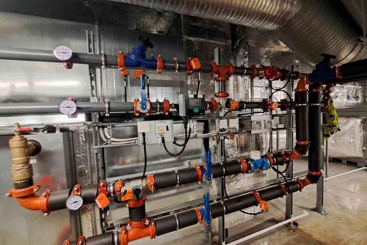 Rørleggersystem med svarte og oransje rør, ventiler og måleinstrumenter i en industriell setting.