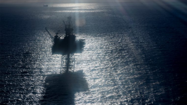 En oljeplattform står silhouett i havet med sollys som reflekteres på vannoverflaten.