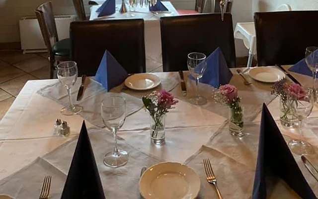 Et dekket bord med hvite duker, glass, tallerkener, bestikk og blomster i små vaser.
