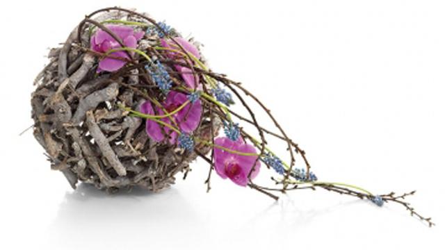 En dekorativ kule laget av kvister, prydet med lilla blomster og lavendel.