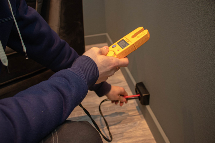 En person bruker en måler for å sjekke elektriske verdier på en vegg i et rom.