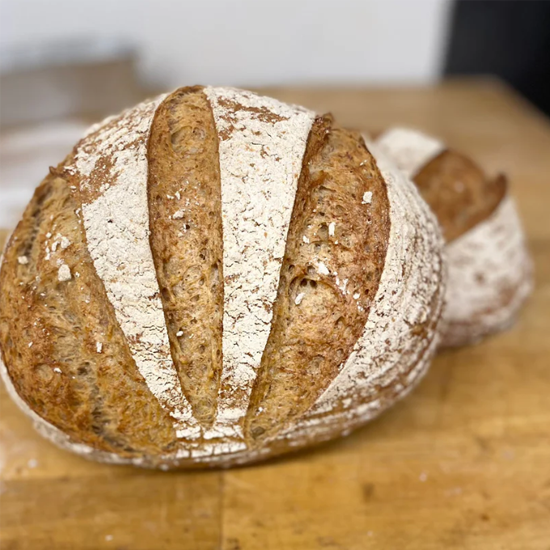 To brød med sprø skorpe og snitt på toppen, plassert på en trebenk.