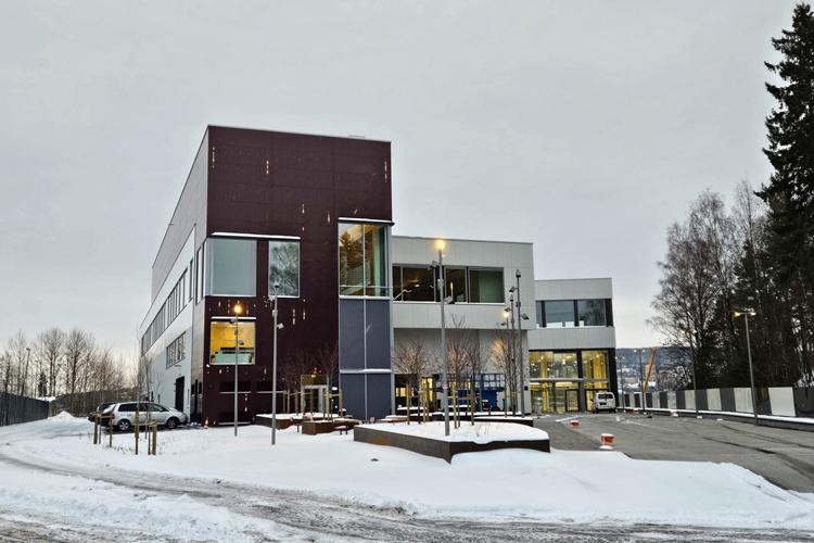 Moderne kontorbygg med snødekt landskap og trær rundt, beliggende i et rolig område.