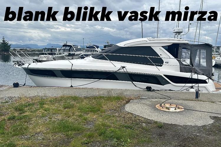 En blank båt ligger ved kaien med flere båter i bakgrunnen under en skyet himmel.