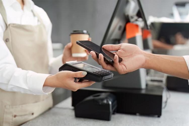 En kunde betaler med mobiltelefon ved kassen, mens en ansatt holder en betalingsenhet.