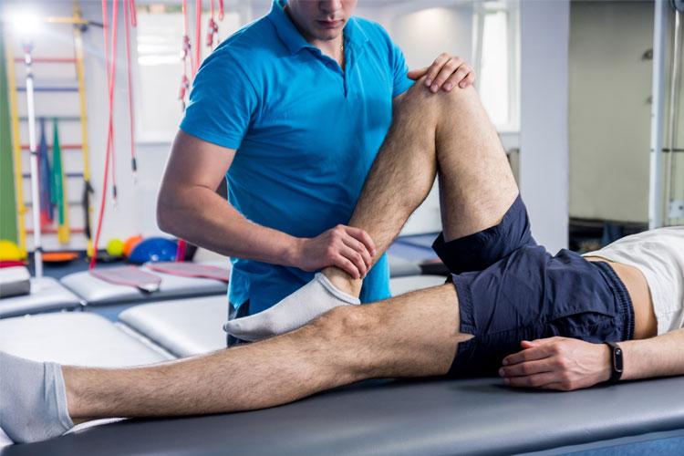 Fysioterapeut som behandler en pasient med benet hevet på en benk i et treningsrom.