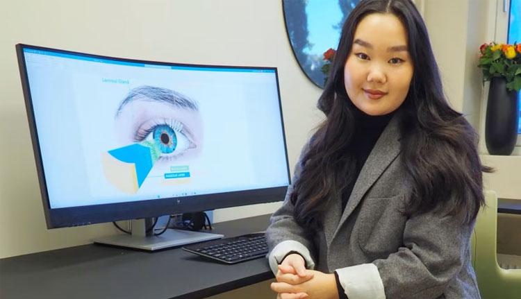 En kvinne med langt, mørkt hår sitter foran en dataskjerm som viser et øye med grafikk.