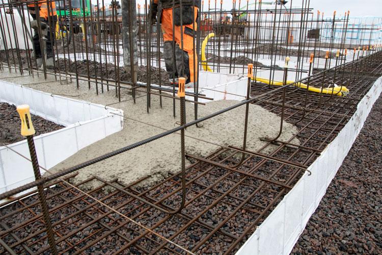 Betonghelling på byggeplass med armeringsjern og arbeidere i bakgrunnen.