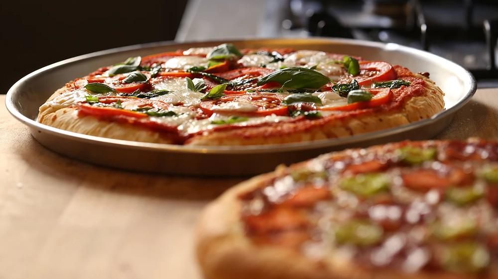 En nybakt pizza med tomatsaus, mozzarella, paprika og basilikum på en metallplate.