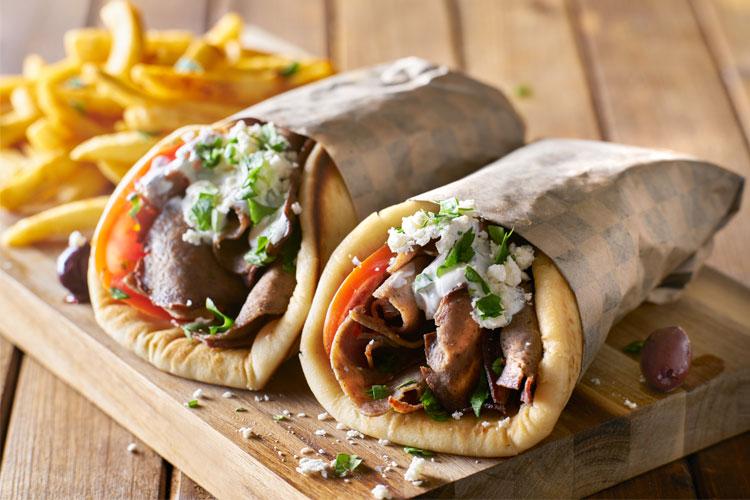 To deilige kebab-wraps med kjøtt, tomat, salat og dressing, servert med pommes frites på en treplate.