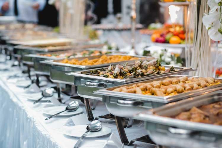 Et variert buffetbord med flere varme retter, inkludert kjøtt, grønnsaker og salater, dekorert med blomster.