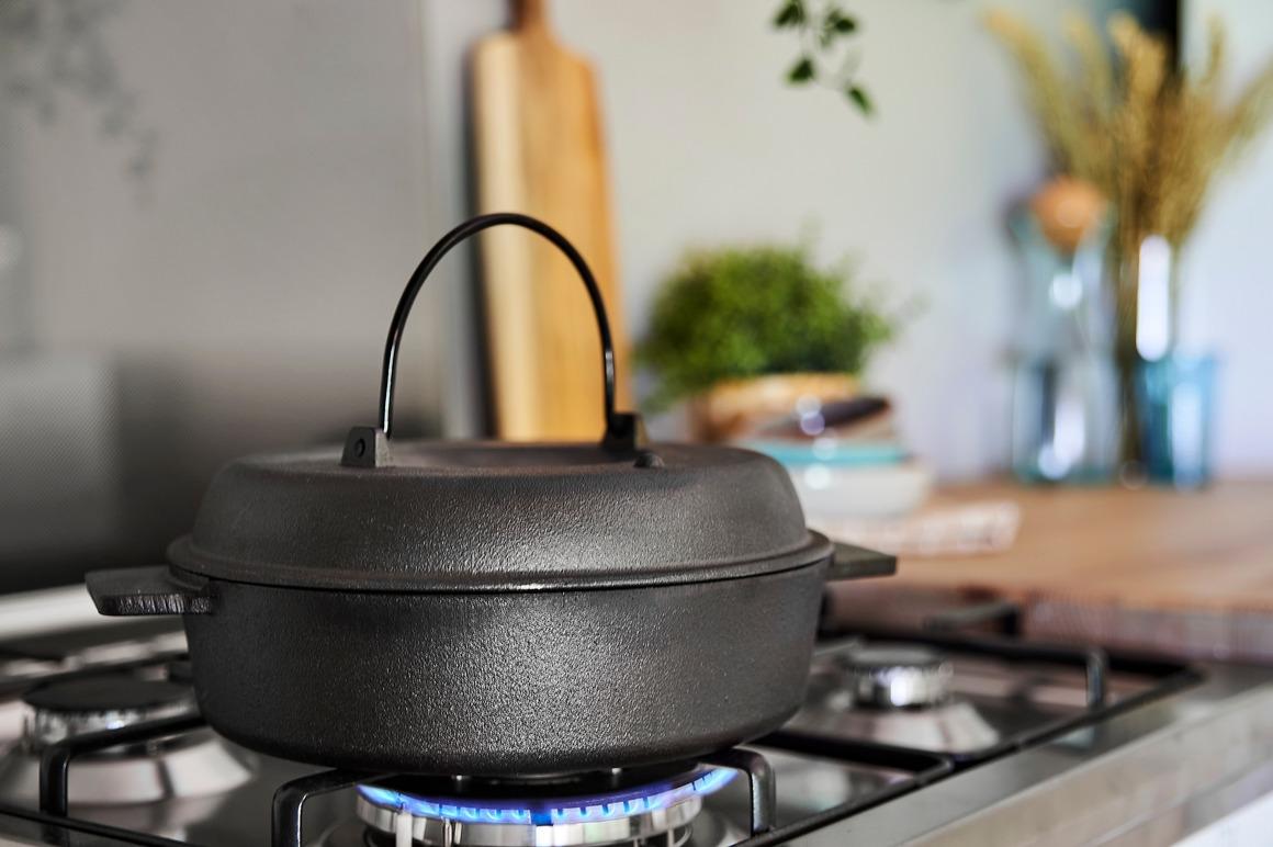 En svart gryte på en gasskomfyr med flammer, i et moderne kjøkkenmiljø.