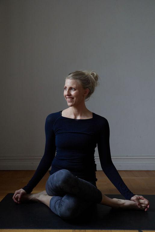 Kvinne som praktiserer yoga i en meditasjonsstilling på en matte, smilende med en avslappet holdning.