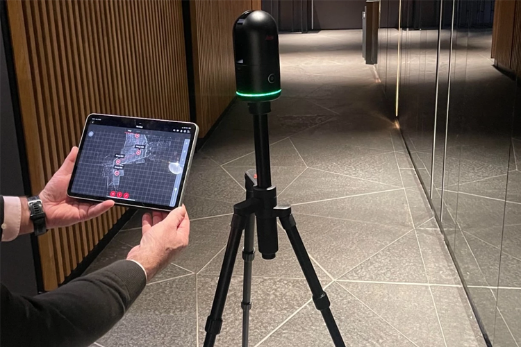 En person bruker en tablet til å kontrollere en 3D-skanner på et stativ i en moderne korridor.
