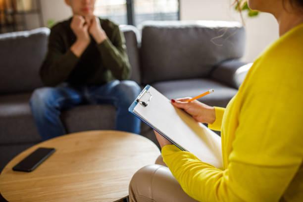 En person sitter på en sofa og snakker med en annen person som skriver notater.