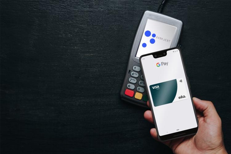 En hånd holder en smarttelefon med Google Pay, ved siden av en betalingsterminal med logoer.