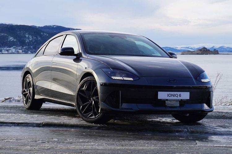 En svart elbil parkert ved vannet med fjell i bakgrunnen, modell KIA EV6.