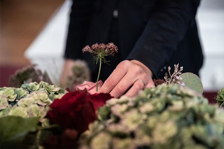 En hånd plasserer en blomst i en bukett med grønne og røde blomster.