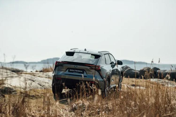 En moderne SUV kjører på en grusvei med tørre gress og fjell i bakgrunnen.