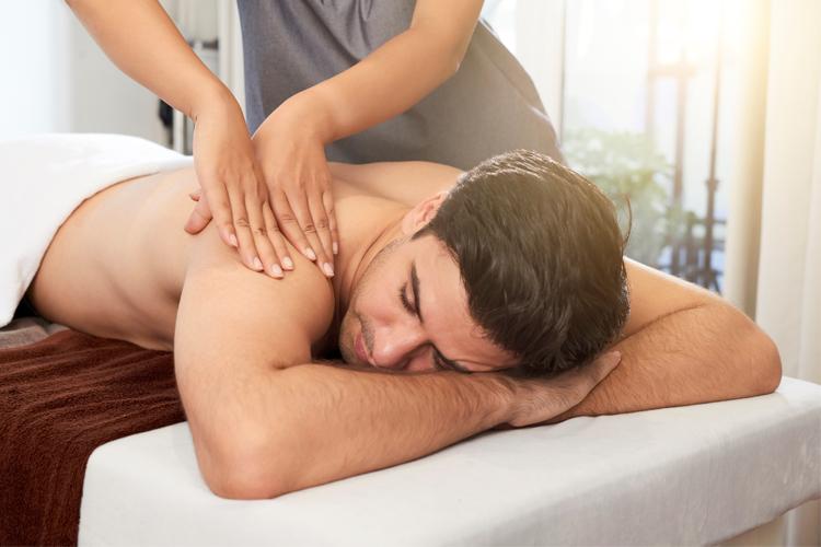 Mann får massasje på en massasjebenk, med en terapeut som masserer skuldrene hans.