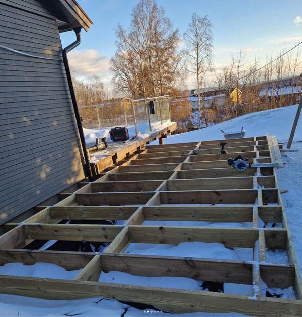 Bilde av en uferdig terrasse med treplanker på snødekt grunn ved siden av et hus.