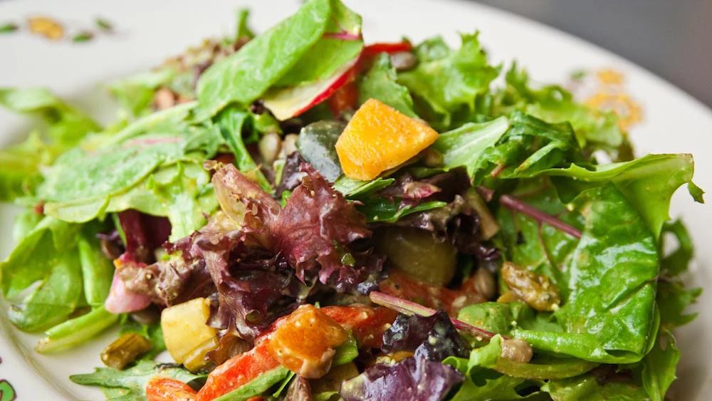 Fargerik salat med blandede grønnsaker, frukt og nøtter på en hvit tallerken.