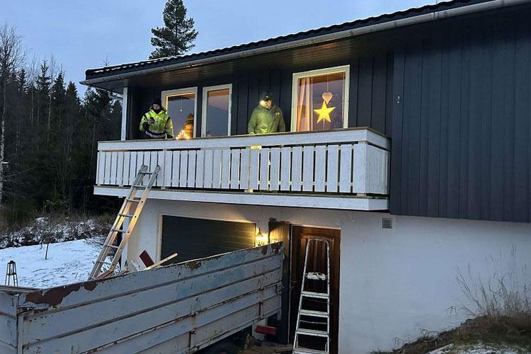 To personer i refleksjakker står på en balkong med stjerner i vinduene, med snø og en lastebil nedenfor.