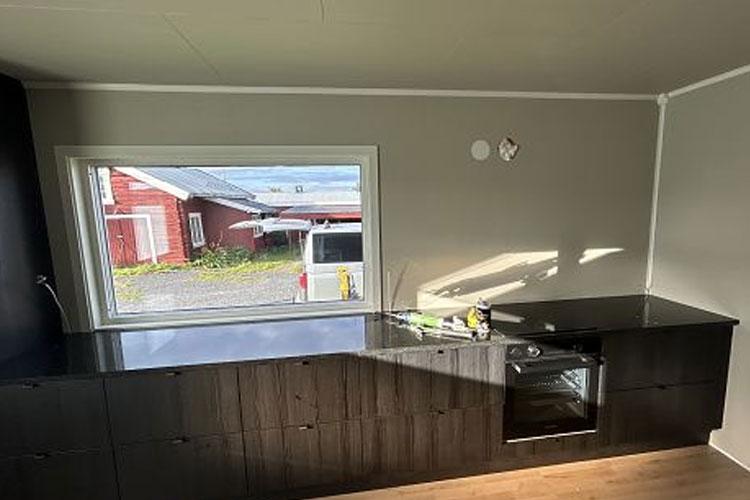 Moderne kjøkken med svart benkeplate, vindu som viser rødt hus og gårdsplass utenfor.