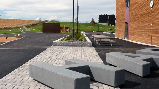Betongbenker og gangsti i et moderne uteområde med grønt landskap i bakgrunnen.