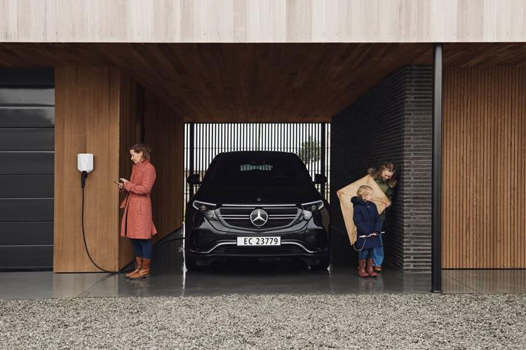 En svart Mercedes EQC lader i en moderne garasje, mens en kvinne og et barn står ved siden av.