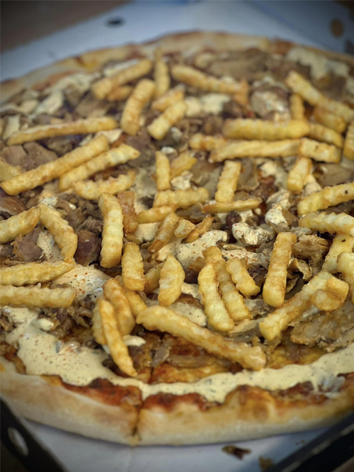 En pizza med kebabkjøtt, hvit saus og sprø pommes frites på toppen.
