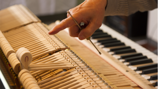En hånd som justerer mekanismen på et piano, med fokus på tangenter og deler av innmaten.