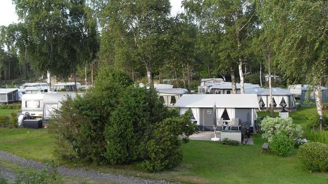 Campingplass med flere campingvogner og hytter omgitt av trær og grøntområde.