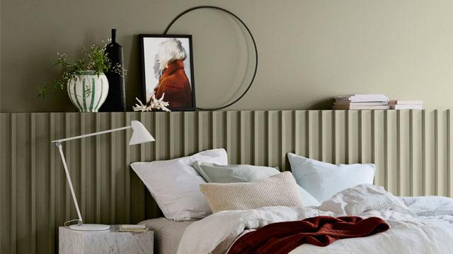 Soverom med grønn vegg, sengetøy i lyse farger, moderne lampe og dekorative elementer på nattbordet.
