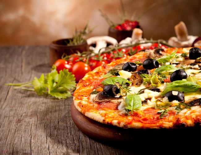 En nybakt pizza med oliven, sopp, tomater og friske urter på et trebord.